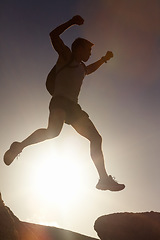 Image showing Man, silhouette and jump on rock at sunset with freedom, adventure and challenge on mountain or cliff. Climbing, hill and person with fearless leap in exercise, sport or energy at with sky in summer