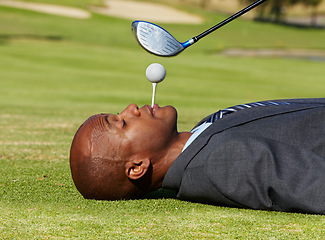 Image showing Black man, face and lying on golf course with tee in mouth for hole in one on green grass or field. African male person, golfer or assistant holding ball with club hovering for swing or hit on pitch