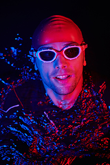 Image showing authentic triathlete swimmer having a break during hard training on night neon gel light