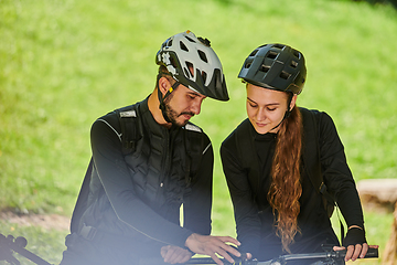 Image showing A blissful couple, adorned in professional cycling gear, enjoys a romantic bicycle ride through a park, surrounded by modern natural attractions, radiating love and happiness