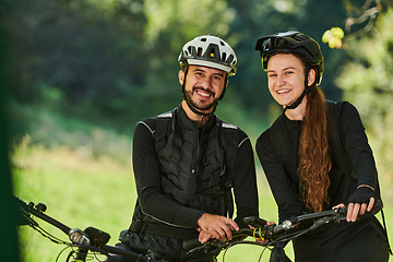 Image showing A blissful couple, adorned in professional cycling gear, enjoys a romantic bicycle ride through a park, surrounded by modern natural attractions, radiating love and happiness