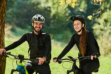 Image showing A blissful couple, adorned in professional cycling gear, enjoys a romantic bicycle ride through a park, surrounded by modern natural attractions, radiating love and happiness