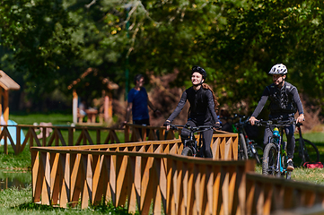 Image showing A blissful couple, adorned in professional cycling gear, enjoys a romantic bicycle ride through a park, surrounded by modern natural attractions, radiating love and happiness