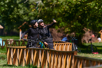 Image showing A blissful couple, adorned in professional cycling gear, enjoys a romantic bicycle ride through a park, surrounded by modern natural attractions, radiating love and happiness