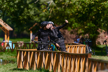 Image showing A blissful couple, adorned in professional cycling gear, enjoys a romantic bicycle ride through a park, surrounded by modern natural attractions, radiating love and happiness