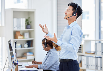Image showing Customer service, man and standing for consulting in call centre with headset, talking and hand gestures. Telemarketing, asian person or financial advisor and employee, computer or happy for helping