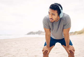 Image showing Man, headphones and break from fitness, beach and exhausted at sea, rest and relaxing for health. Male person, wellness and music for cardio, workout and tired from training, streaming radio or song