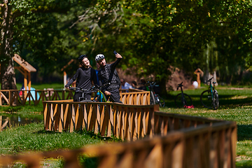 Image showing A blissful couple, adorned in professional cycling gear, enjoys a romantic bicycle ride through a park, surrounded by modern natural attractions, radiating love and happiness