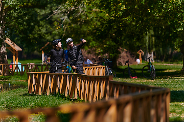 Image showing A blissful couple, adorned in professional cycling gear, enjoys a romantic bicycle ride through a park, surrounded by modern natural attractions, radiating love and happiness