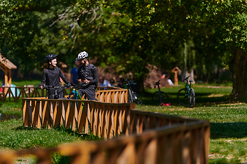 Image showing A blissful couple, adorned in professional cycling gear, enjoys a romantic bicycle ride through a park, surrounded by modern natural attractions, radiating love and happiness