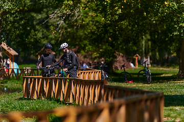 Image showing A blissful couple, adorned in professional cycling gear, enjoys a romantic bicycle ride through a park, surrounded by modern natural attractions, radiating love and happiness