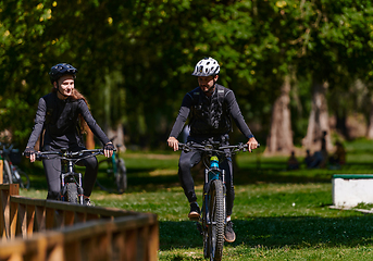 Image showing A blissful couple, adorned in professional cycling gear, enjoys a romantic bicycle ride through a park, surrounded by modern natural attractions, radiating love and happiness