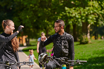 Image showing A blissful couple, adorned in professional cycling gear, enjoys a romantic bicycle ride through a park, surrounded by modern natural attractions, radiating love and happiness