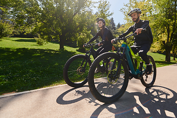 Image showing A blissful couple, adorned in professional cycling gear, enjoys a romantic bicycle ride through a park, surrounded by modern natural attractions, radiating love and happiness