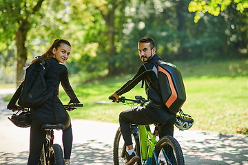 Image showing A blissful couple, adorned in professional cycling gear, enjoys a romantic bicycle ride through a park, surrounded by modern natural attractions, radiating love and happiness