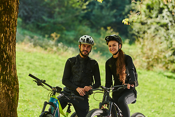 Image showing A blissful couple, adorned in professional cycling gear, enjoys a romantic bicycle ride through a park, surrounded by modern natural attractions, radiating love and happiness