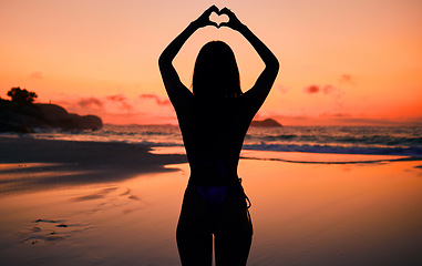 Image showing Woman, silhouette and sunset by water with heart hands for love, care and kindness with sign, summer and body. Girl, person and beach with symbol, emoji or icon on vacation, ocean or outdoor at dusk