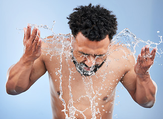 Image showing Black man, water splash and face wash for skincare, hygiene or grooming against a blue studio background. African male person, model and aqua for body hydration, shower or facial skin treatment