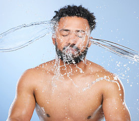 Image showing Black man, water splash and washing in skincare for cleaning, hygiene or grooming against a blue studio background. Face of African male person, model and aqua for body hydration, shower or skin wash