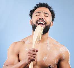 Image showing Shower, brush and man singing in studio for cleaning, wellness or morning routine on blue background. Bathroom, karaoke and male model having fun with body scrubber, cosmetics or luxury washing