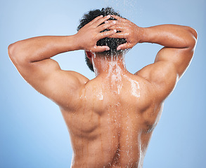 Image showing Man, shower back and wash in studio with water, splash or hygiene with self care by blue background. Person, guy and muscle with hair, wellness or health for skin, natural dermatology and body