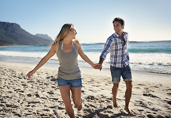 Image showing Happy couple, holding hands and walk on beach, vacation and freedom in summer sunshine with bonding. Man, woman and running with smile, care and love by sand, waves and outdoor on holiday in Napoli