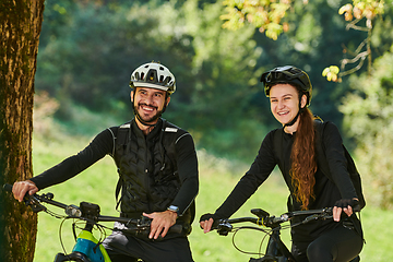 Image showing A blissful couple, adorned in professional cycling gear, enjoys a romantic bicycle ride through a park, surrounded by modern natural attractions, radiating love and happiness