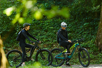 Image showing A blissful couple, adorned in professional cycling gear, enjoys a romantic bicycle ride through a park, surrounded by modern natural attractions, radiating love and happiness