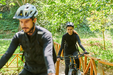 Image showing A blissful couple, adorned in professional cycling gear, enjoys a romantic bicycle ride through a park, surrounded by modern natural attractions, radiating love and happiness