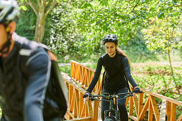 Image showing A blissful couple, adorned in professional cycling gear, enjoys a romantic bicycle ride through a park, surrounded by modern natural attractions, radiating love and happiness