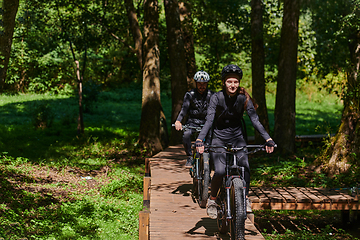 Image showing A blissful couple, adorned in professional cycling gear, enjoys a romantic bicycle ride through a park, surrounded by modern natural attractions, radiating love and happiness