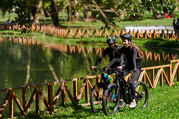 Image showing A blissful couple, adorned in professional cycling gear, enjoys a romantic bicycle ride through a park, surrounded by modern natural attractions, radiating love and happiness