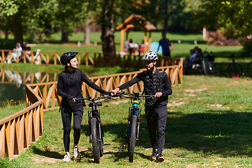 Image showing A blissful couple, adorned in professional cycling gear, enjoys a romantic bicycle ride through a park, surrounded by modern natural attractions, radiating love and happiness