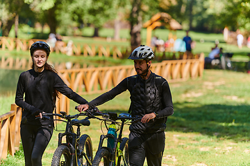 Image showing A blissful couple, adorned in professional cycling gear, enjoys a romantic bicycle ride through a park, surrounded by modern natural attractions, radiating love and happiness