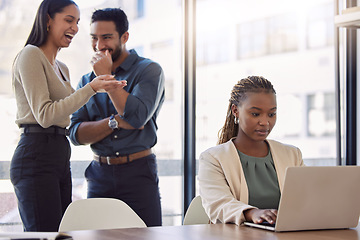 Image showing Office bully, woman and working at laptop with coworkers laughing in a corporate workplace about gossip. Young black person typing on a computer with internet and joke with staff being mean at desk