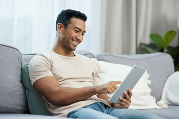 Image showing Tablet, smile and relax with a man on a sofa in the living room of his home for social media browsing. Technology, app or gaming search with a happy young person in his apartment on the weekend