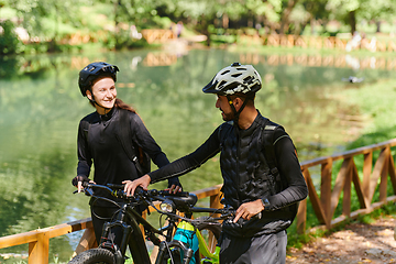 Image showing A blissful couple, adorned in professional cycling gear, enjoys a romantic bicycle ride through a park, surrounded by modern natural attractions, radiating love and happiness