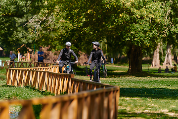 Image showing A blissful couple, adorned in professional cycling gear, enjoys a romantic bicycle ride through a park, surrounded by modern natural attractions, radiating love and happiness