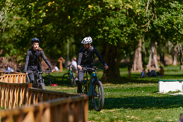 Image showing A blissful couple, adorned in professional cycling gear, enjoys a romantic bicycle ride through a park, surrounded by modern natural attractions, radiating love and happiness