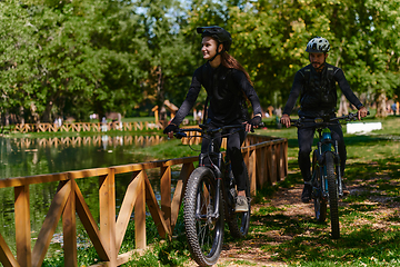 Image showing A blissful couple, adorned in professional cycling gear, enjoys a romantic bicycle ride through a park, surrounded by modern natural attractions, radiating love and happiness