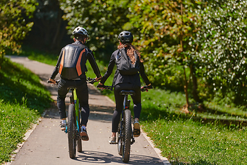 Image showing A blissful couple, adorned in professional cycling gear, enjoys a romantic bicycle ride through a park, surrounded by modern natural attractions, radiating love and happiness