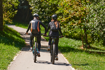 Image showing A blissful couple, adorned in professional cycling gear, enjoys a romantic bicycle ride through a park, surrounded by modern natural attractions, radiating love and happiness