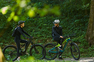 Image showing A blissful couple, adorned in professional cycling gear, enjoys a romantic bicycle ride through a park, surrounded by modern natural attractions, radiating love and happiness