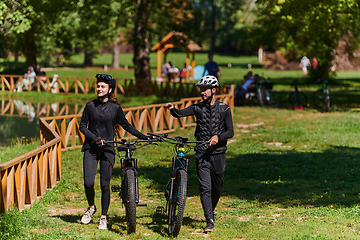 Image showing A blissful couple, adorned in professional cycling gear, enjoys a romantic bicycle ride through a park, surrounded by modern natural attractions, radiating love and happiness