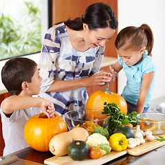 Image showing Mom, daughter and son with pumpkins for halloween in the kitchen of their home for holiday celebration. Family, food or tradition and a woman teaching her kids how to carve vegetables in an apartment