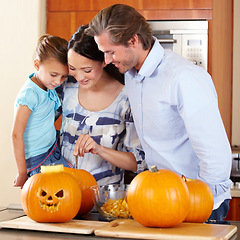 Image showing Halloween, pumpkin and a family in the kitchen of their house together for holiday celebration. Creative, smile or happy with a mom, dad and daughter carving a face into a vegetable for decoration