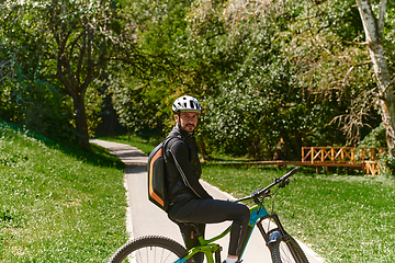 Image showing In the radiant glow of a sunny day, a fitness enthusiast, donned in professional gear, pedals through the park on his bicycle, embodying strength and vitality in a dynamic outdoor workout