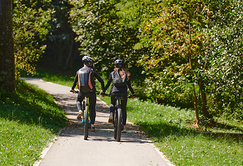 Image showing A blissful couple, adorned in professional cycling gear, enjoys a romantic bicycle ride through a park, surrounded by modern natural attractions, radiating love and happiness