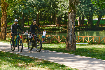 Image showing A blissful couple, adorned in professional cycling gear, enjoys a romantic bicycle ride through a park, surrounded by modern natural attractions, radiating love and happiness