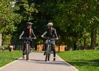 Image showing A blissful couple, adorned in professional cycling gear, enjoys a romantic bicycle ride through a park, surrounded by modern natural attractions, radiating love and happiness